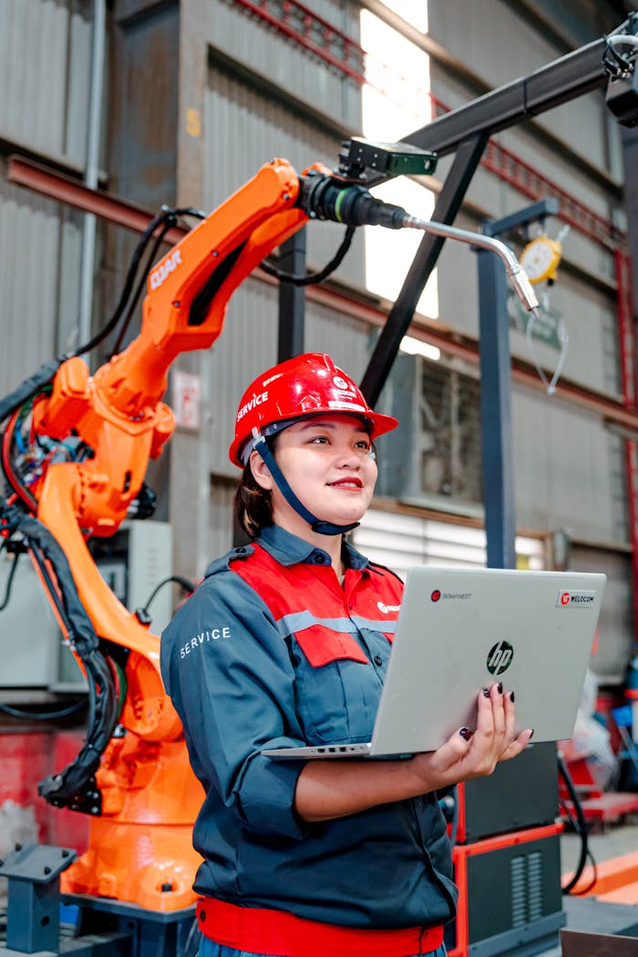 Female engineer with laptop overseeing robotic arm in a manufacturing setting in Vietnam.